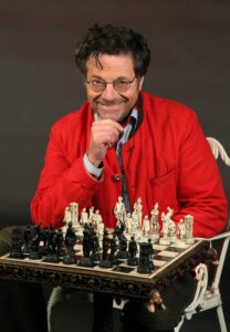Portraitfoto Dr. Diether Dehm in roter Jacke mit Schachbrett vor sich